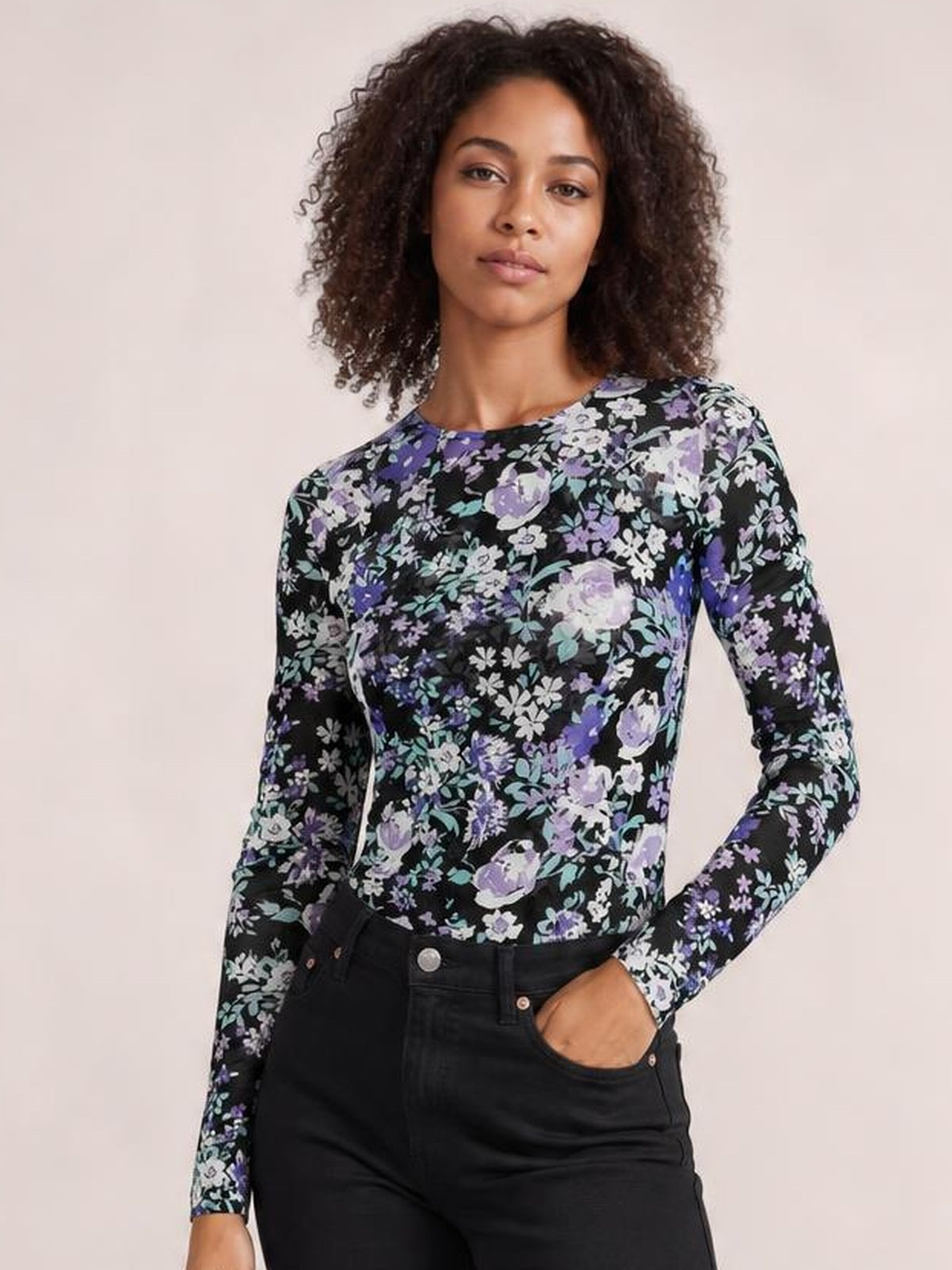 Model poses with one hand in her pocket wearing a black floral round neck long sleeve T-shirt with a fitted silhouette and slight stretch.