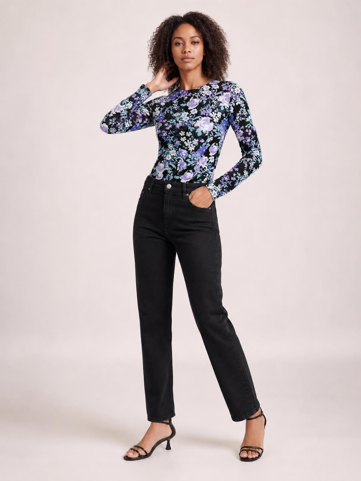 Model poses in a floral round neck long sleeve T-shirt with a fitted silhouette, black base, and purple, blue, and white flower print.