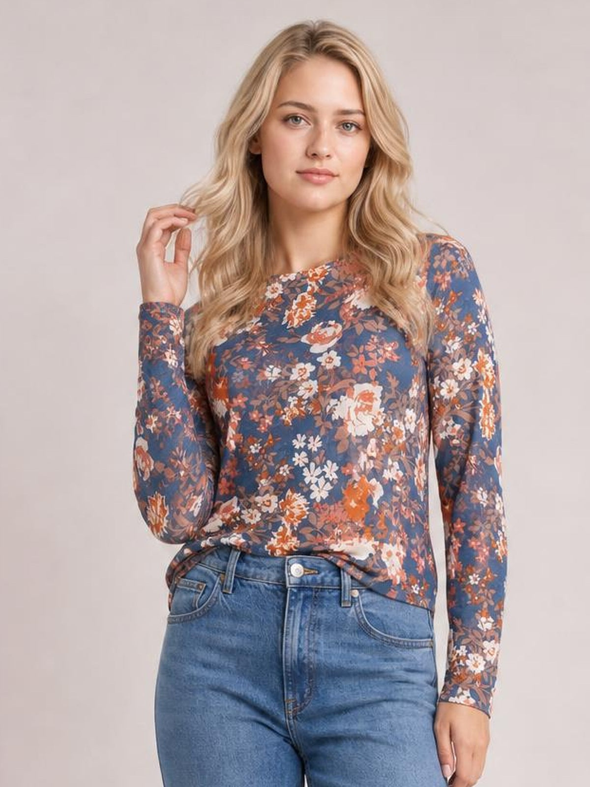 Model poses in a blue floral round neck long sleeve T-shirt with a fitted silhouette, slightly stretchy construction, and one hand touching her hair.
