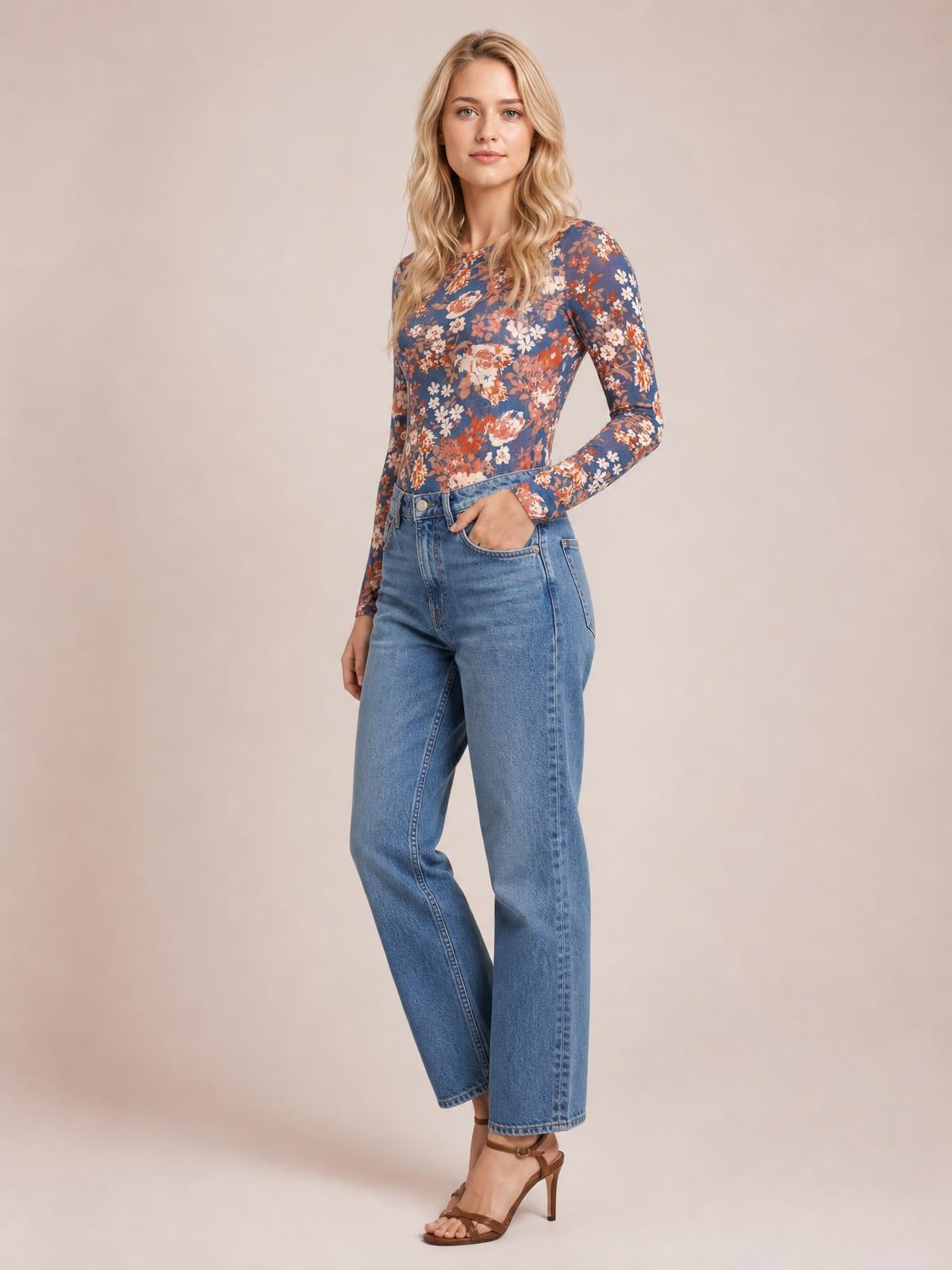 A model poses with one hand in her jeans pocket, wearing a fitted blue floral round-neck T-shirt with long sleeves and a stretchy silhouette.