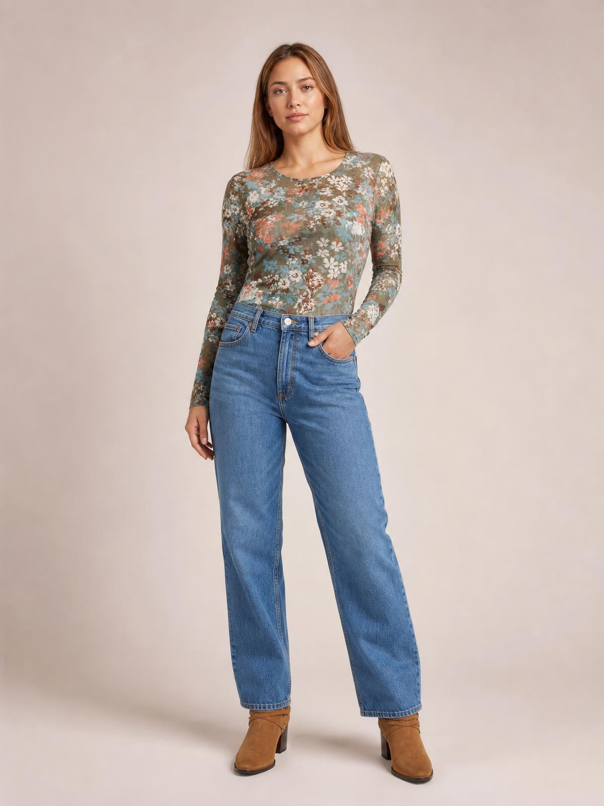 Model poses in a fitted floral round neck long sleeve T-shirt with muted green, blue, coral, and white flowers, paired with jeans and one hand in a pocket.