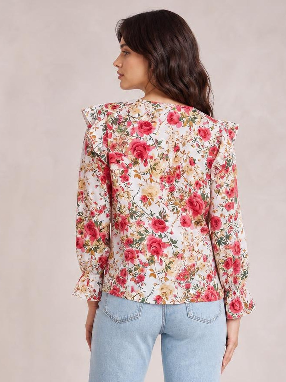A model looks over her shoulder in a floral round-neck blouse with a white base, pink and red flowers, long sleeves, and a relaxed straight silhouette.