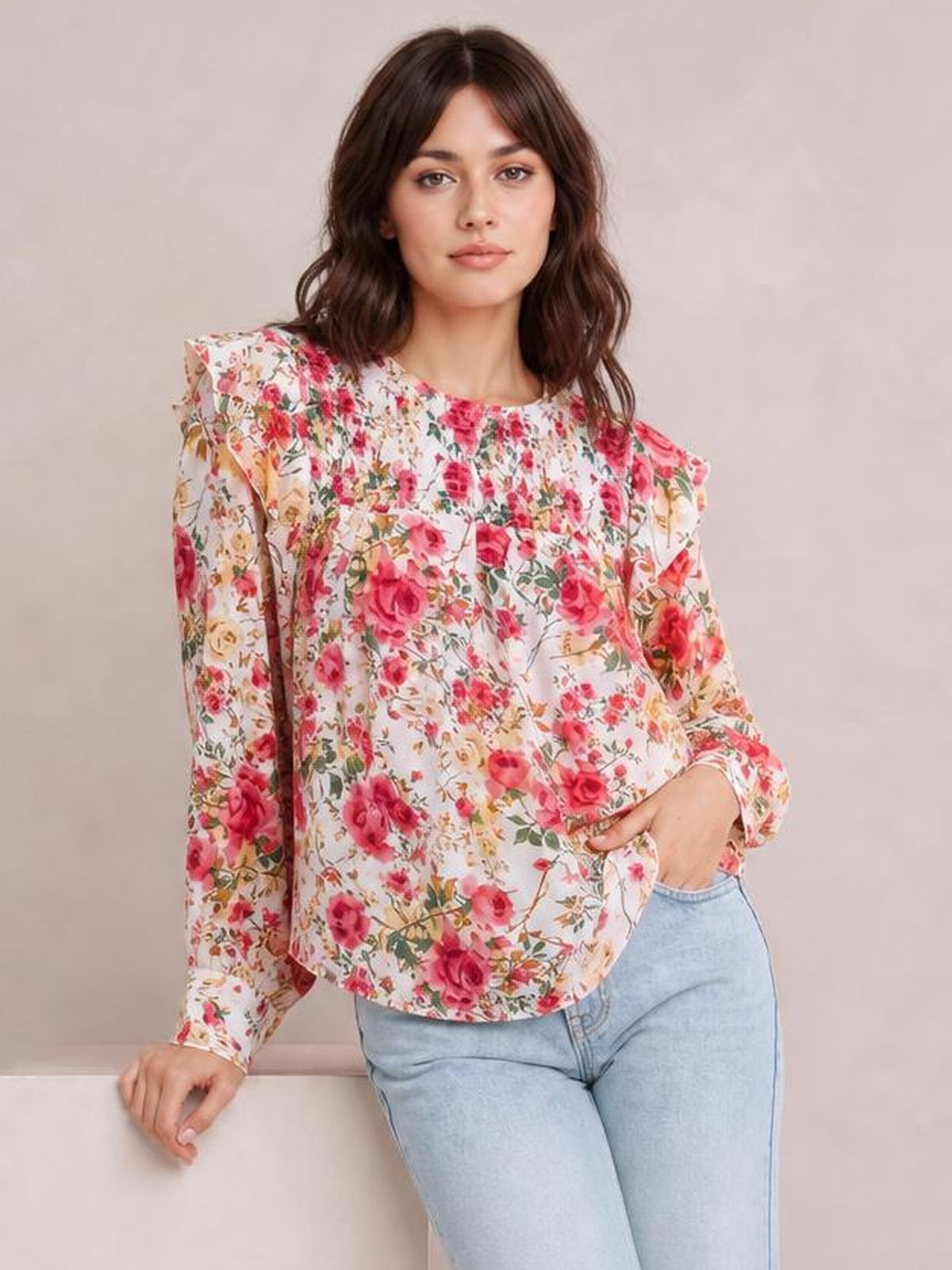 A model poses in a white floral round-neck smocked blouse with long sleeves, a relaxed silhouette, and pink, red, and green flower print.