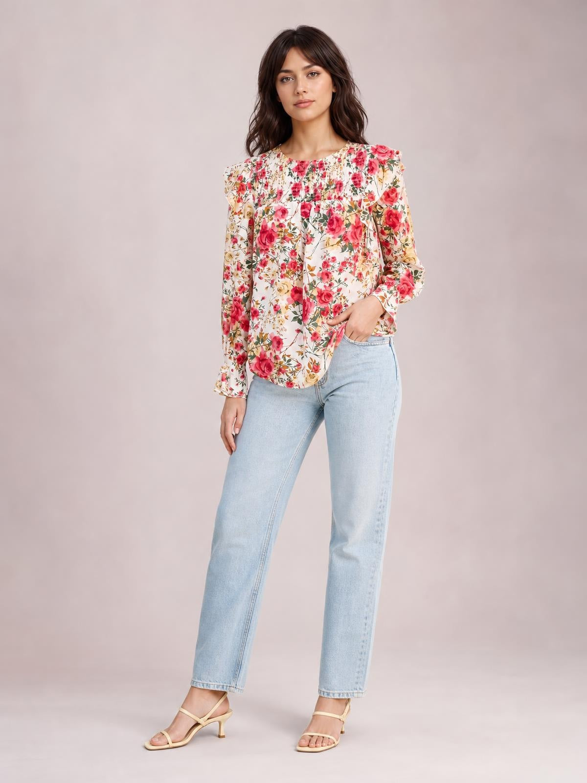 Model stands with one hand in her jeans pocket, wearing a cream floral smocked blouse with a round neck, long sleeves, and a relaxed silhouette.