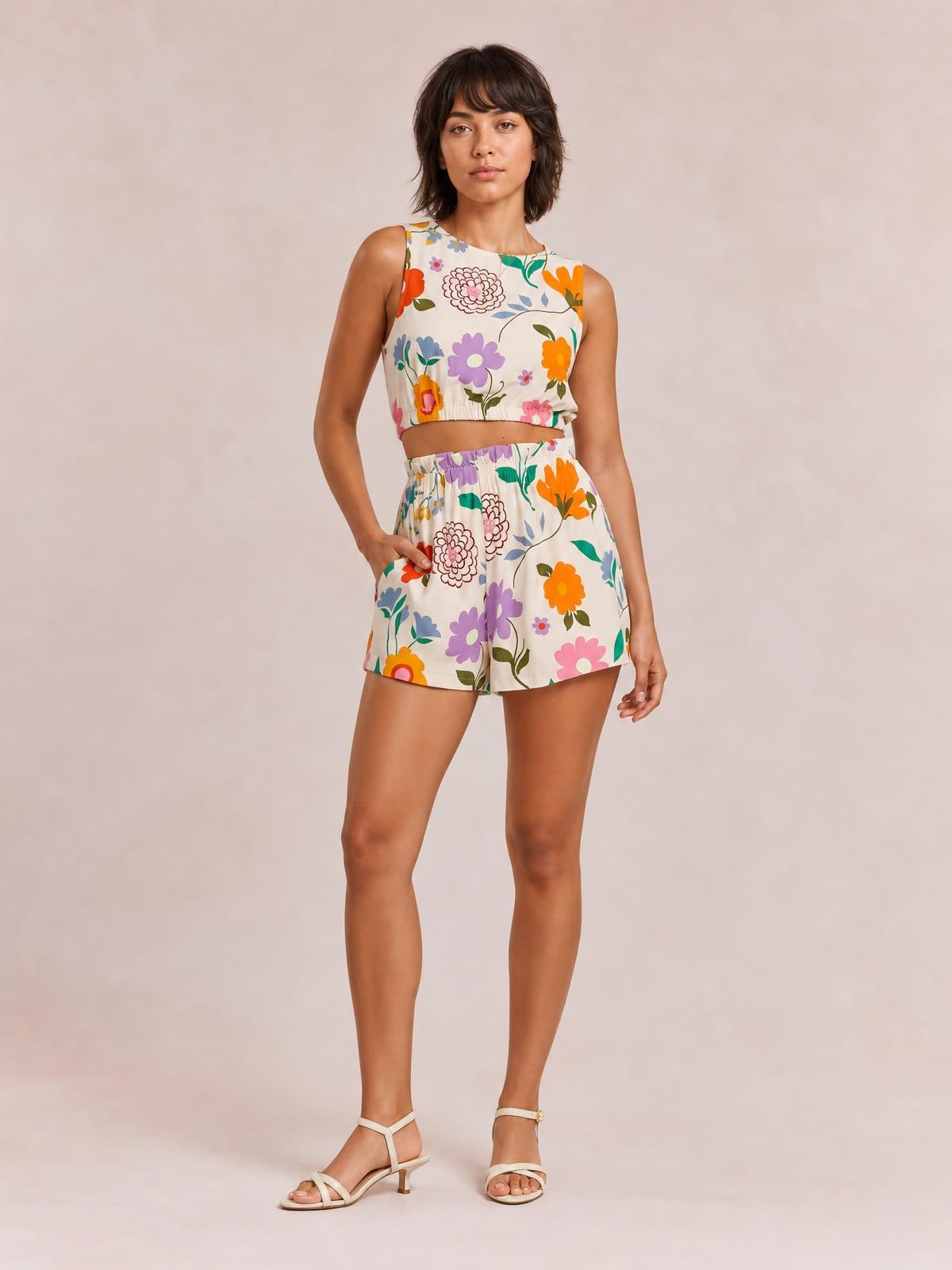 Model poses in a floral round neck tank and shorts set with a cropped ruched hem, colorful print, relaxed shorts silhouette, and a visible pocket.