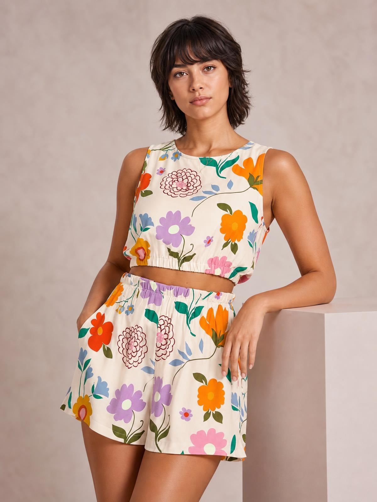 Model poses in a colorful floral round neck tank and shorts set with a cropped ruched hem, elastic waistband, relaxed shorts silhouette, and side pockets.
