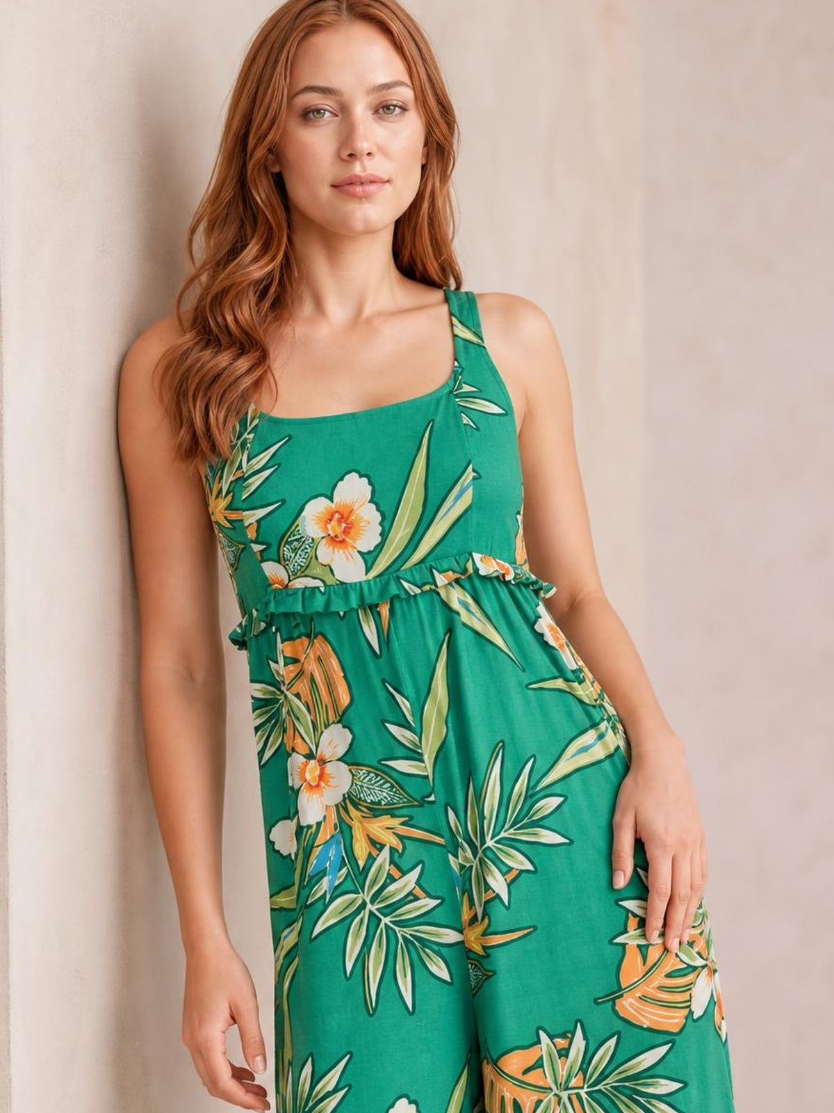 Model poses in a green floral sleeveless jumpsuit with wide legs, a square neckline, and a ruffled waist detail.