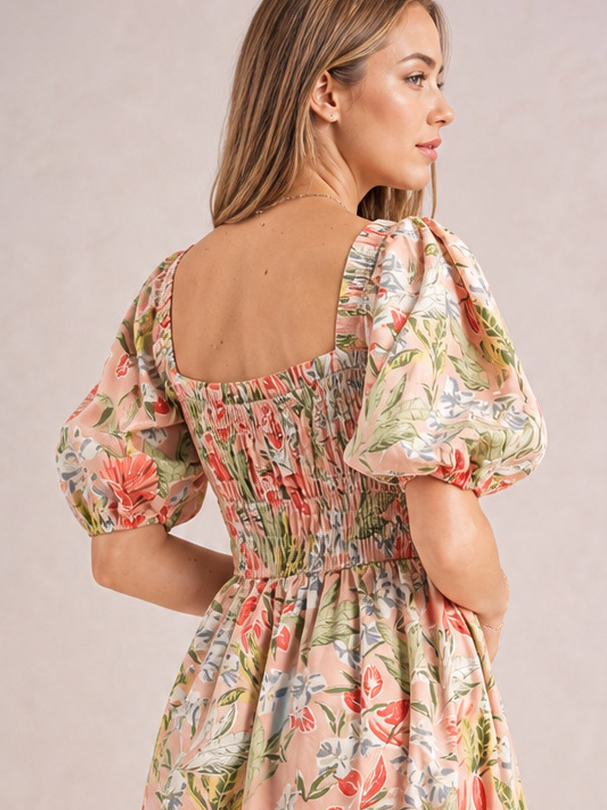 Model shown from behind in a pink floral smocked midi dress with a square back neckline, puff short sleeves, gathered waist, and flowing skirt.