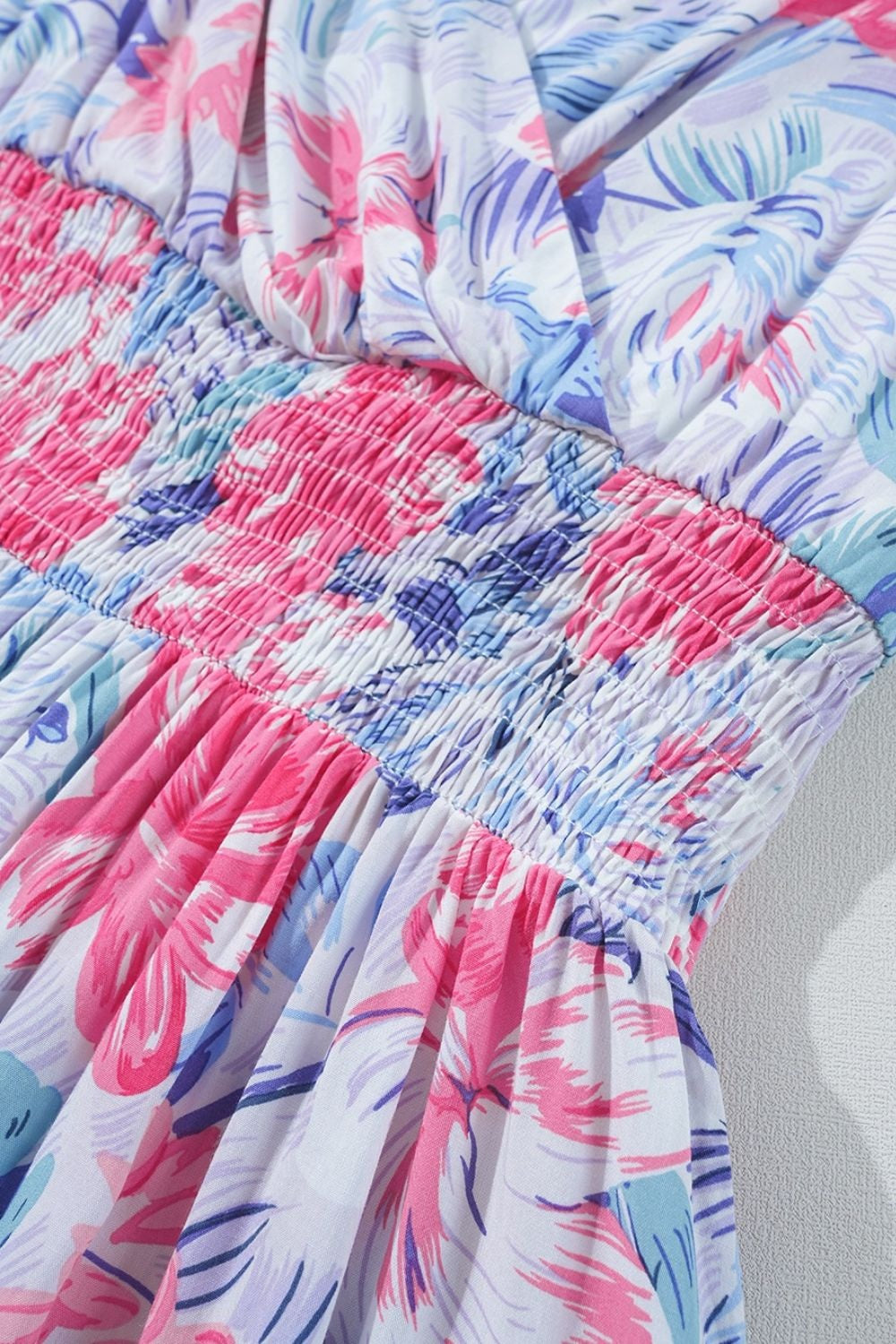 Close-up of a pastel floral mini dress showing its shirred waist, gathered construction, and flowing pink, blue, and lavender fabric.