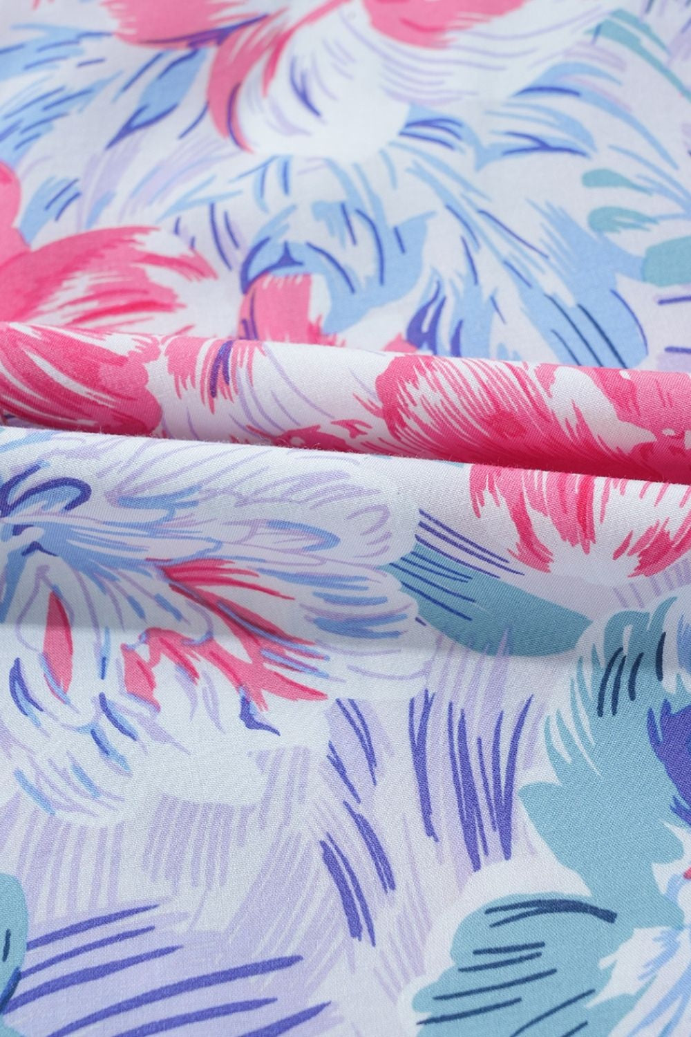 Close-up of the mini dress fabric shows a light base with abstract pink, blue, lavender, and teal floral brushstroke print.