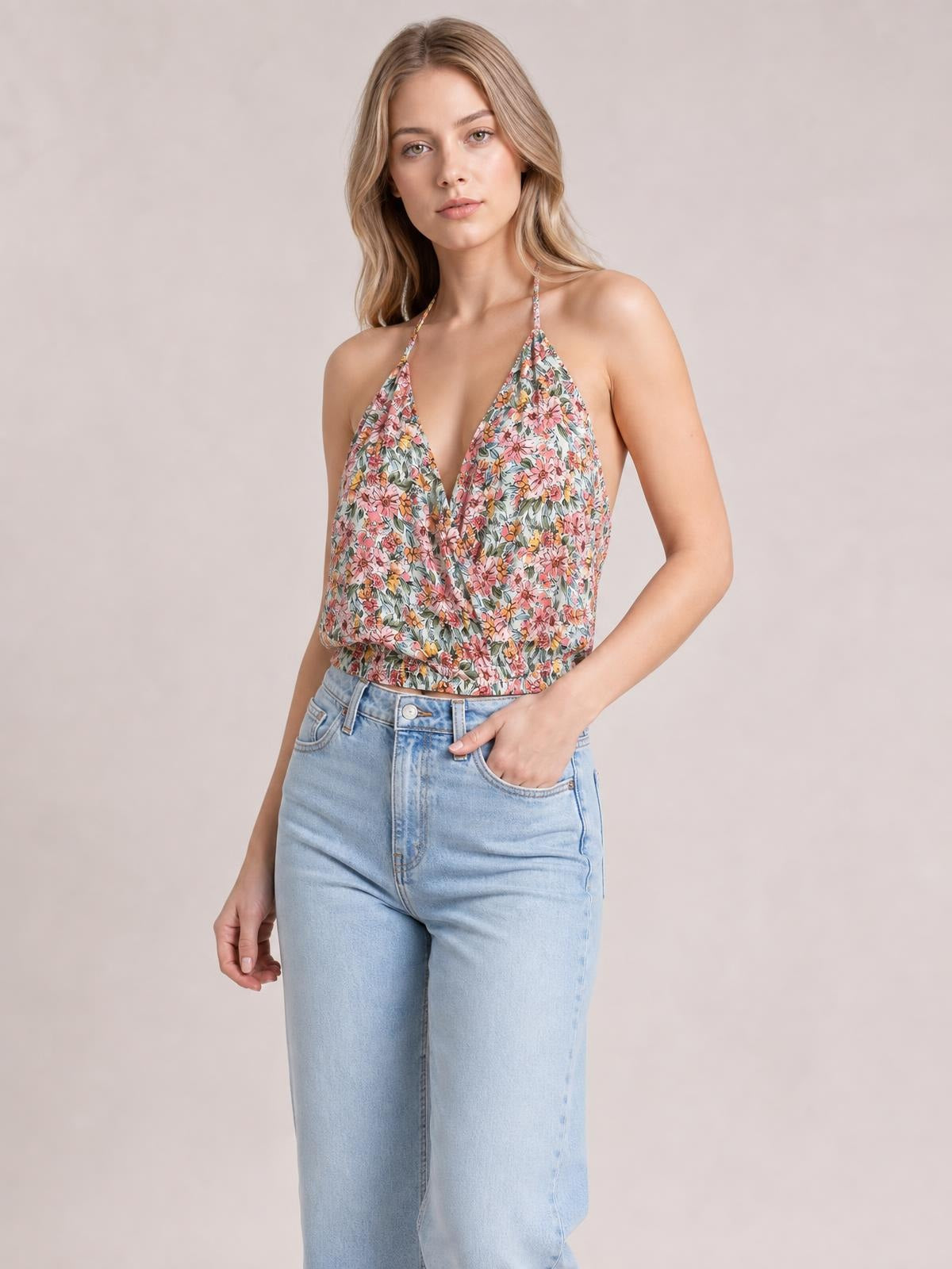 A model poses with one hand in her jeans pocket wearing a multicolor floral surplice-neck cami with thin straps, a sleeveless silhouette, and a gathered hem.