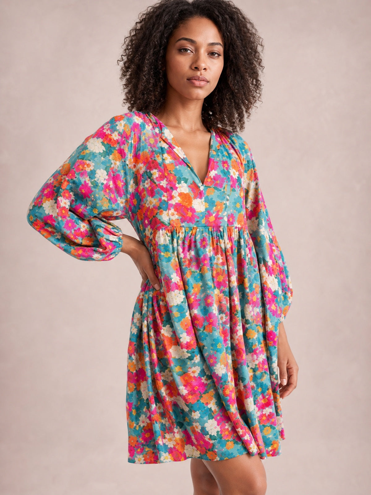 Model poses in a vibrant teal floral mini dress with pink, orange, and white blooms, a tied V-neck, puff sleeves, gathered waist, and flared skirt.