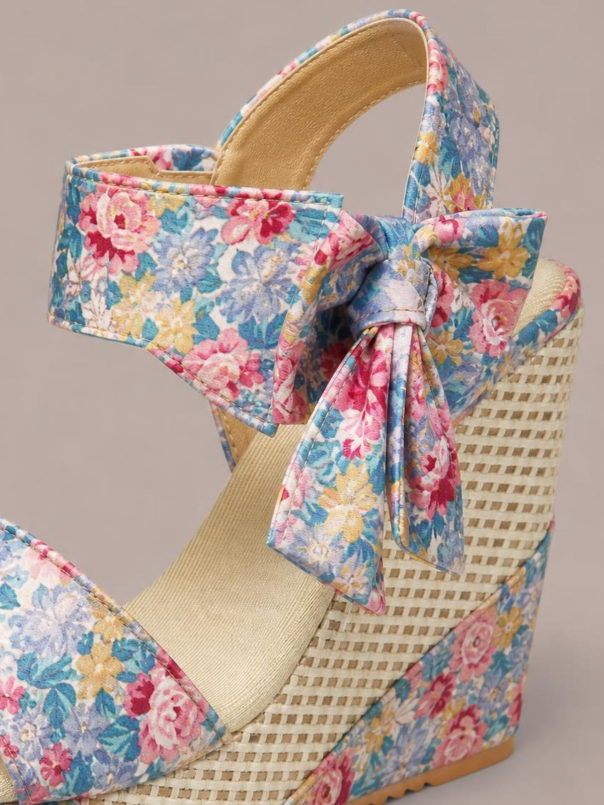 Floral tied high heel sandal with a multicolor flower print, oversized bow detail, broad straps, and a tall woven wedge silhouette.