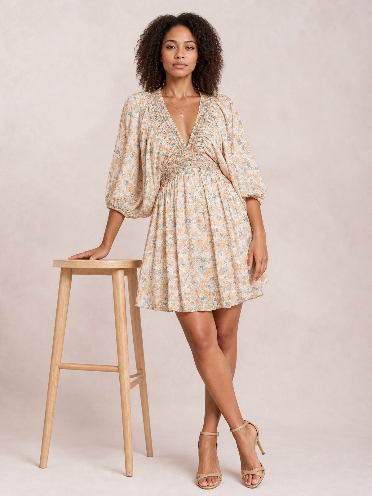 Model poses in a floral V-neck mini dress with a softly gathered waist, voluminous balloon sleeves, ruched detailing, and a gently flared skirt.