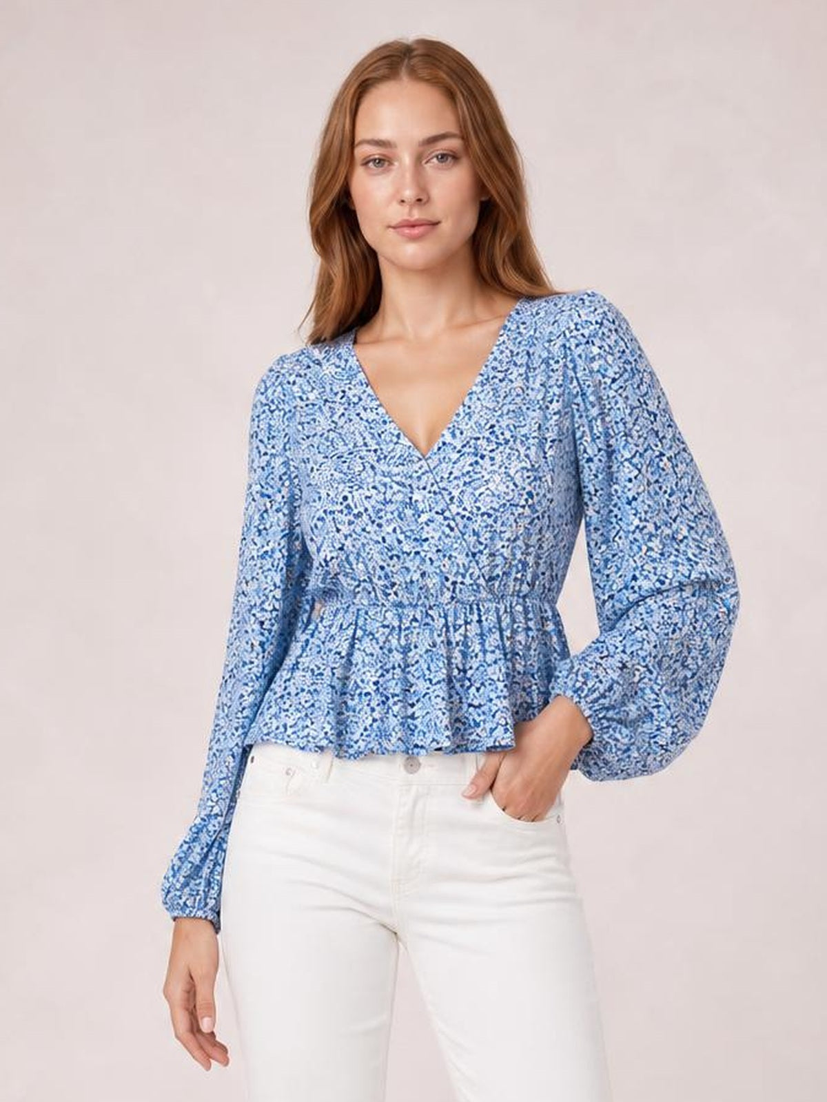 A model stands in a blue floral V-neck peplum blouse with gathered waist, flared hem, and long balloon sleeves, one hand in her pocket.