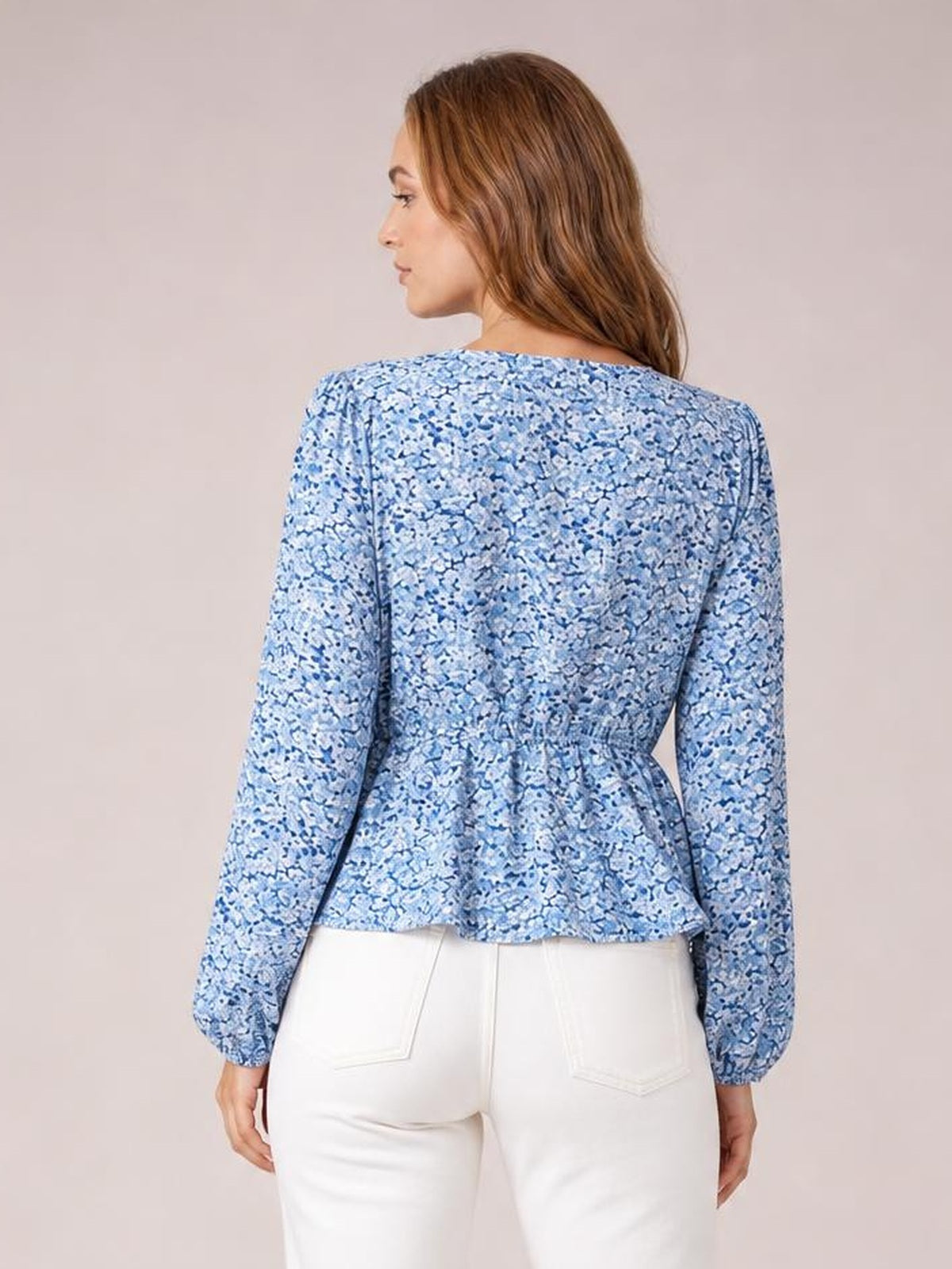 Model shown from the back wears a blue floral blouse with long balloon sleeves, a fitted waist, and a flared peplum hem over white pants.