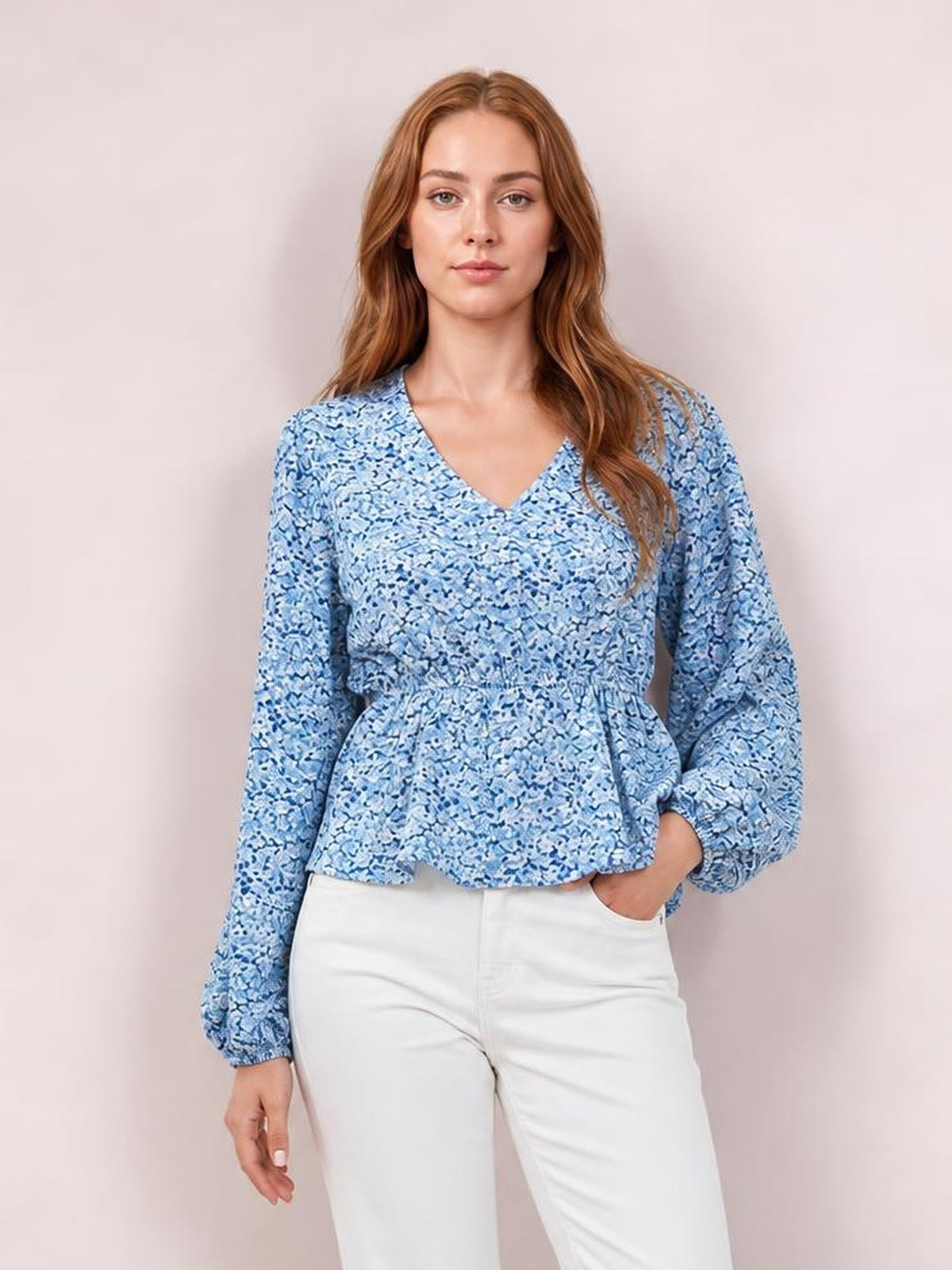 Model poses in a blue floral V-neck peplum blouse with voluminous balloon sleeves, gathered waist seam, and flared hem.