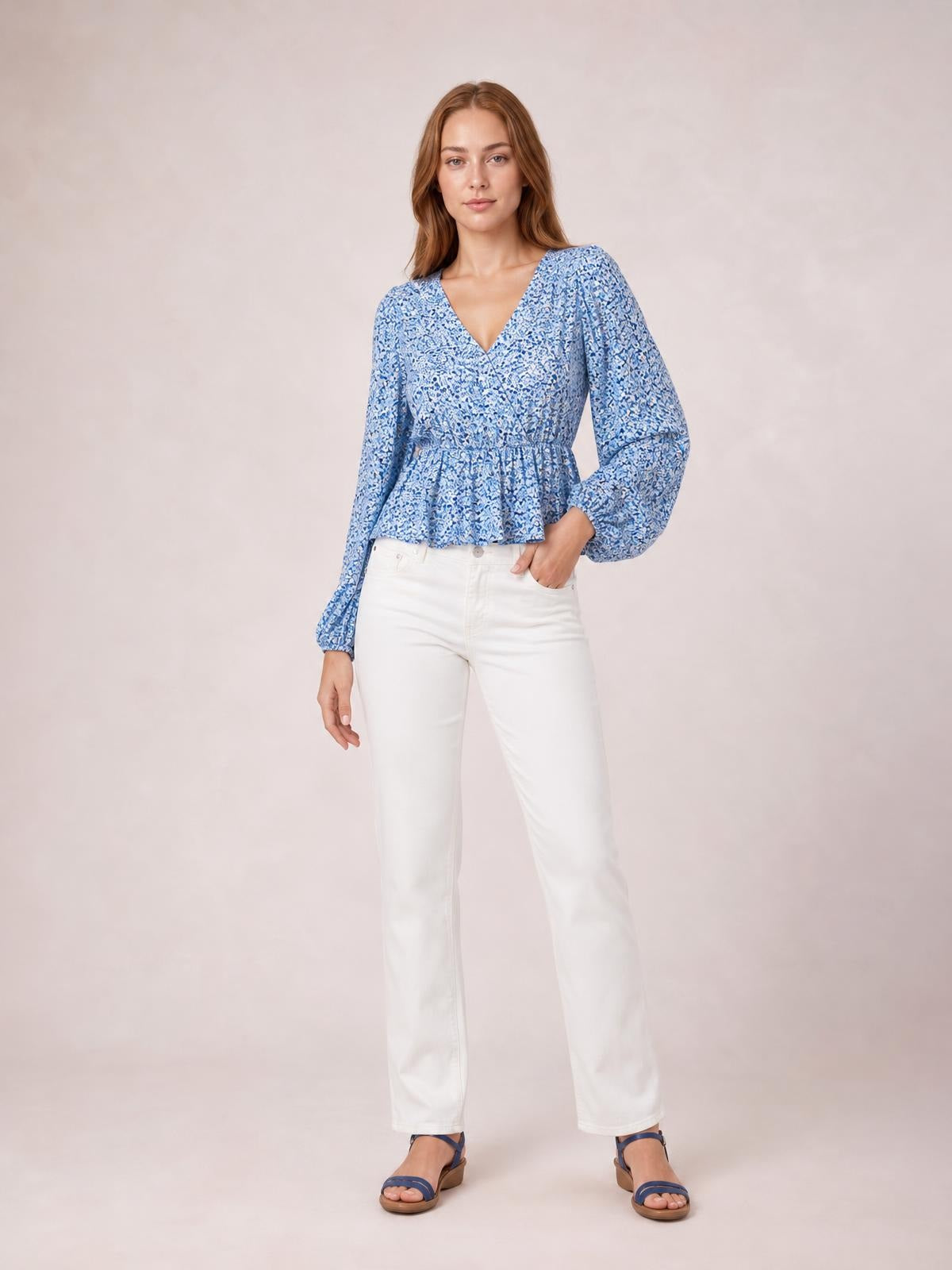 A model stands in a blue floral V-neck peplum blouse with voluminous balloon sleeves, a gathered waist, and a flared hem.