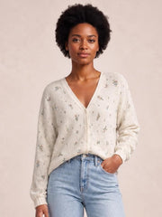 Model wears an ivory floral V-neck button-down cardigan with a relaxed silhouette, long sleeves, ribbed cuffs, and front buttons, posing with one hand in her jeans pocket.