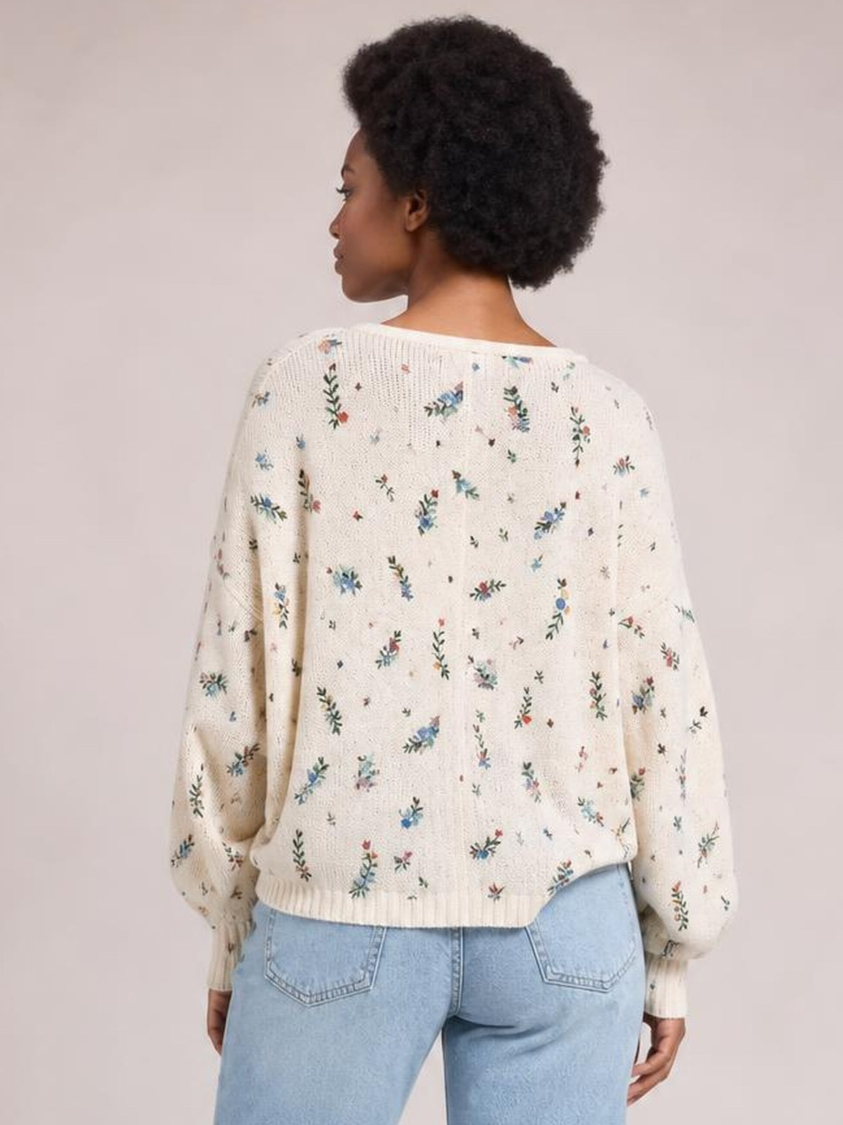 A model shows the back of a cream floral cardigan with a relaxed silhouette, long sleeves, textured knit construction, and ribbed cuffs and hem.