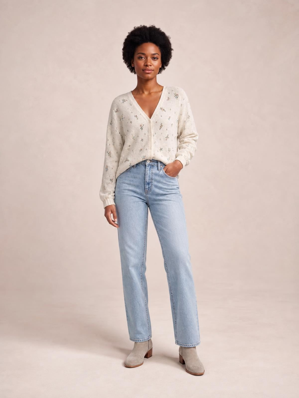 Model standing in a cream floral V-neck button-down cardigan with long sleeves, ribbed cuffs, and a relaxed silhouette, one hand in her jeans pocket.