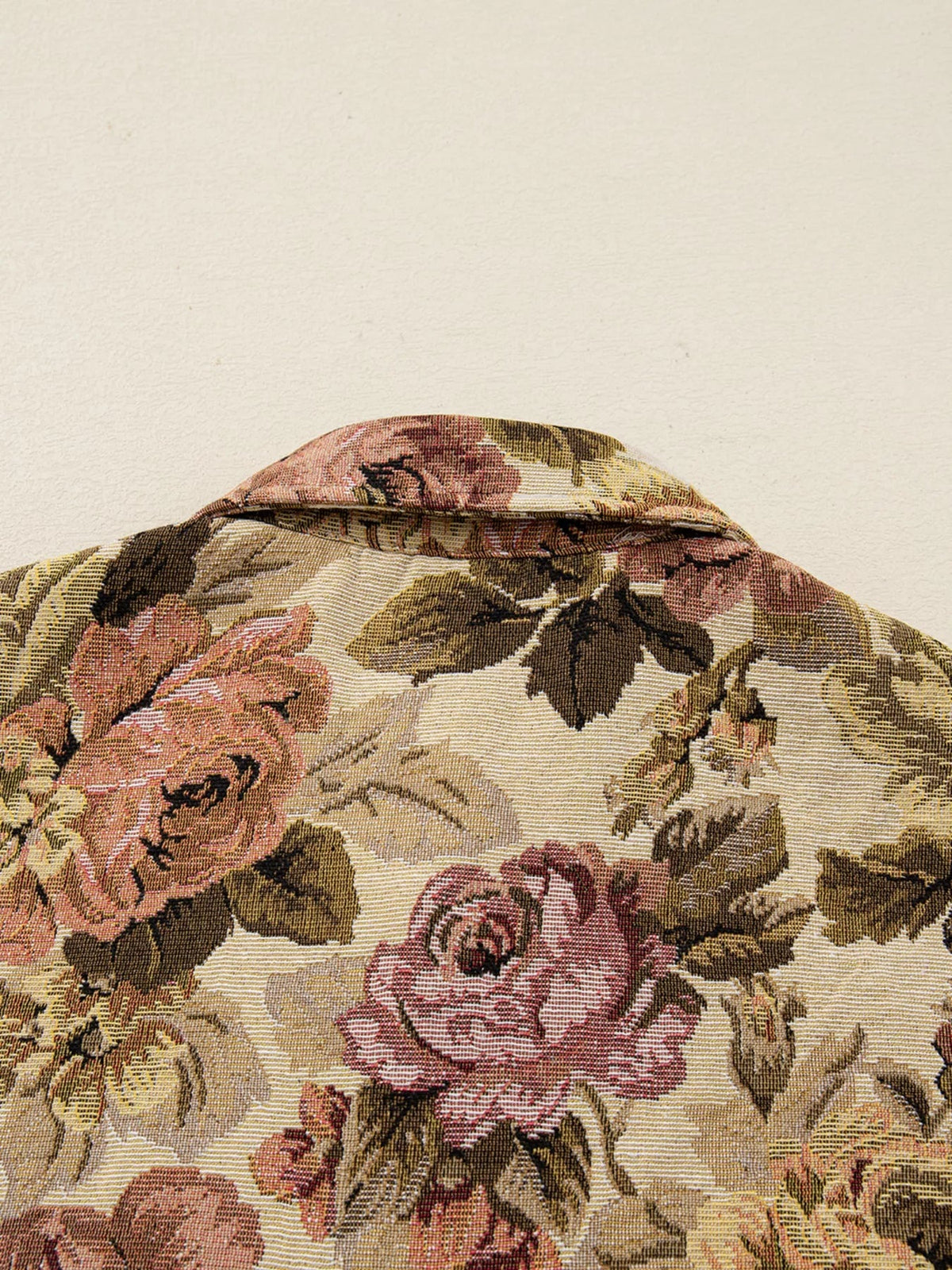 Close-up of a floral waffle-knit jacket showing a textured patchwork pattern in muted pink, brown, olive, and cream with a structured collar.