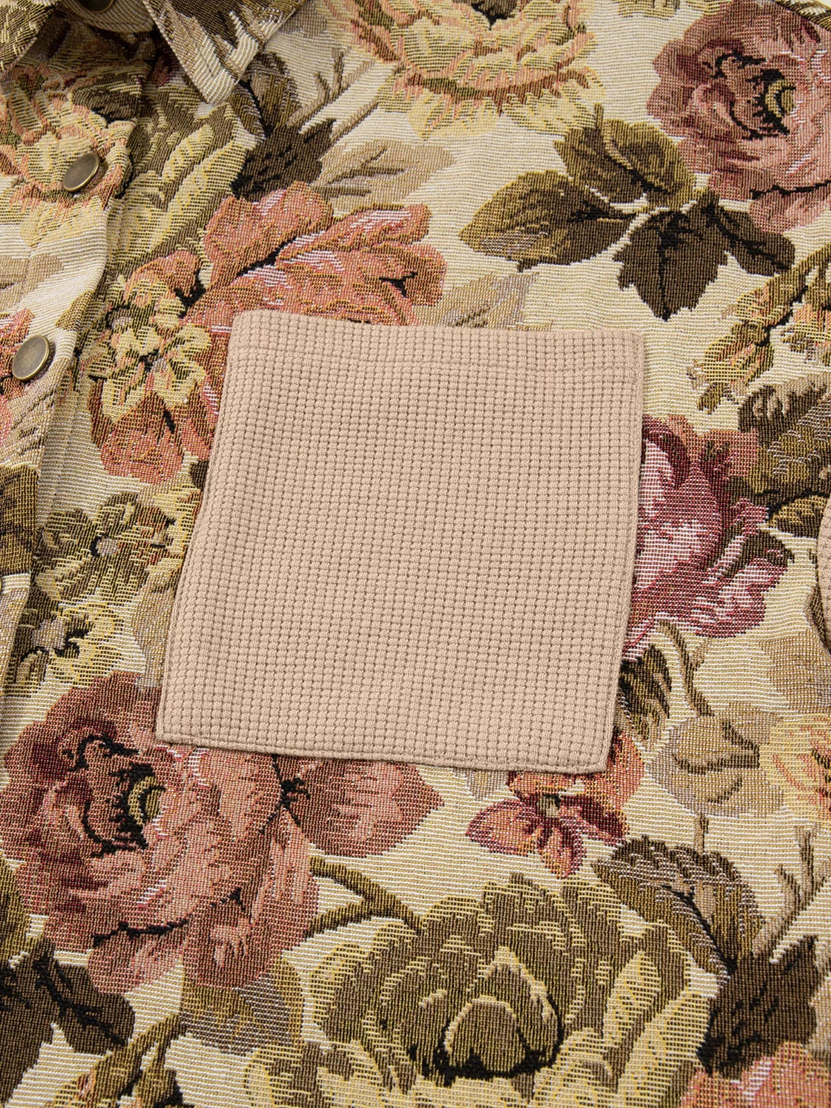 Close-up of a floral jacket showing its textured waffle knit patch pocket, button fastening, and muted pink, beige, olive, and brown woven pattern.