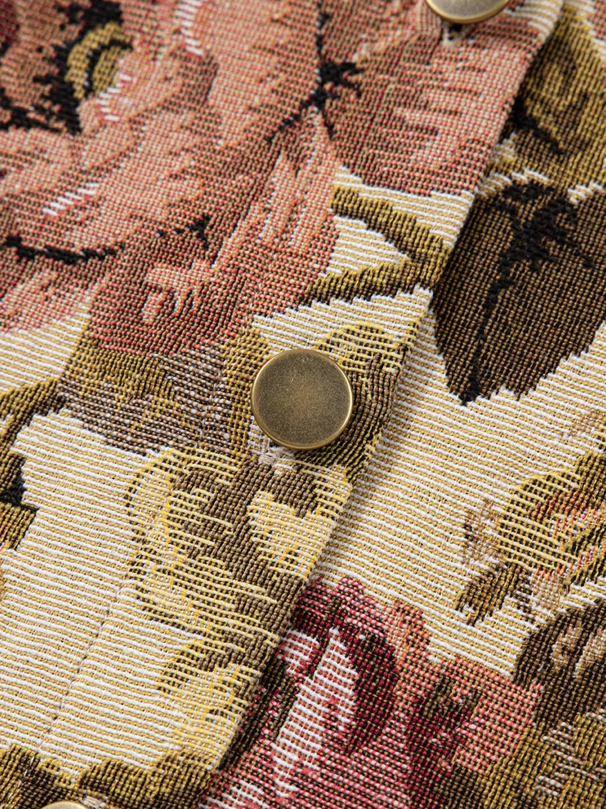 Close-up of a floral patchwork jacket in textured red, mustard, black, and cream fabric, featuring visible stitching and round bronze-tone buttons.