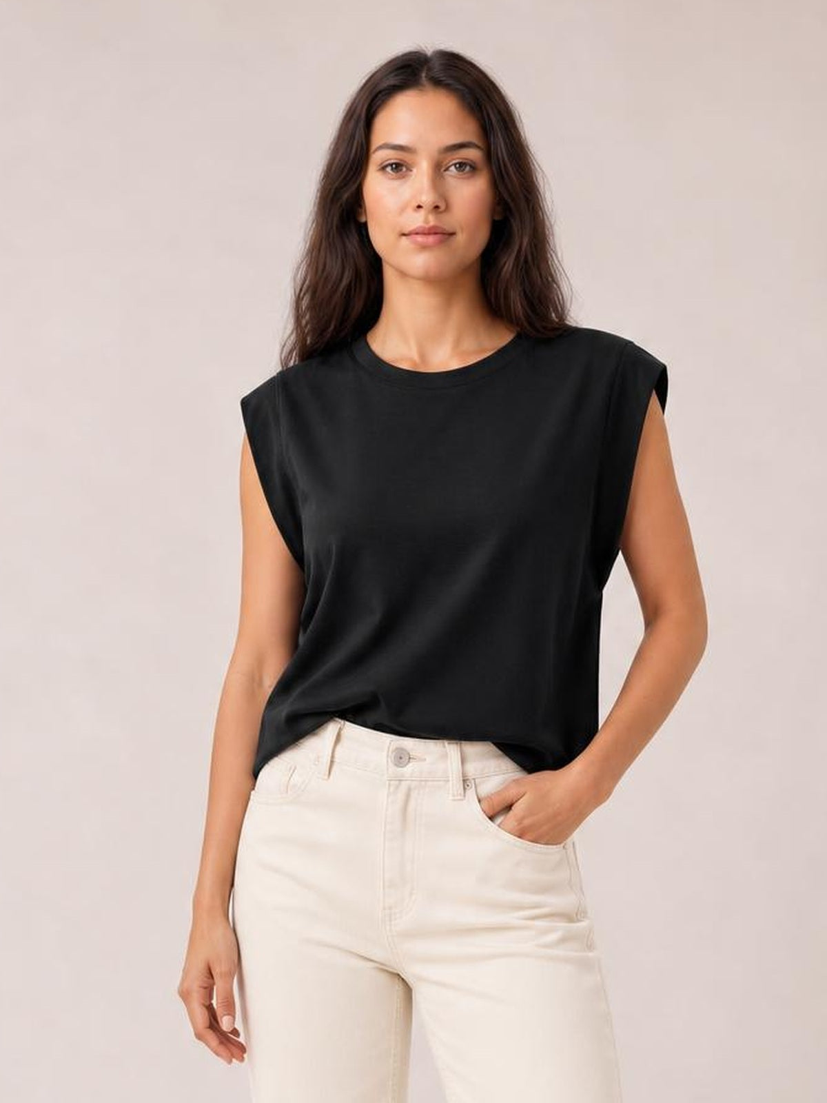 A model stands in a black Florira T-shirt with a round neck, cap sleeves, and a relaxed silhouette, pairing it with light pants and one hand in a pocket.