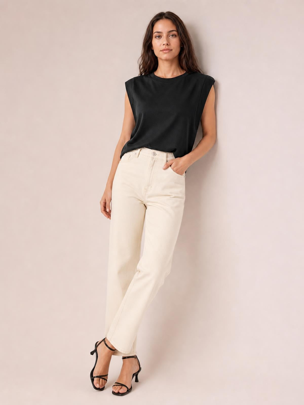 A model poses in a black Florira round neck cap sleeve T-shirt with a relaxed silhouette, lightly draped construction, one hand in her pocket and crossed legs.