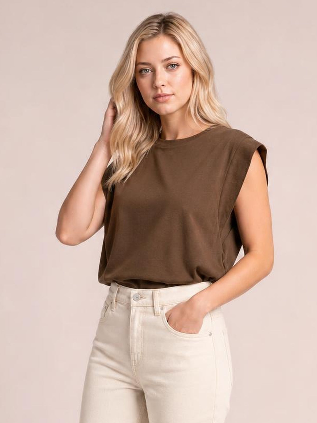 Model poses in a brown Florira round neck cap sleeve T-shirt with a relaxed silhouette, tucked into high-waisted white jeans.