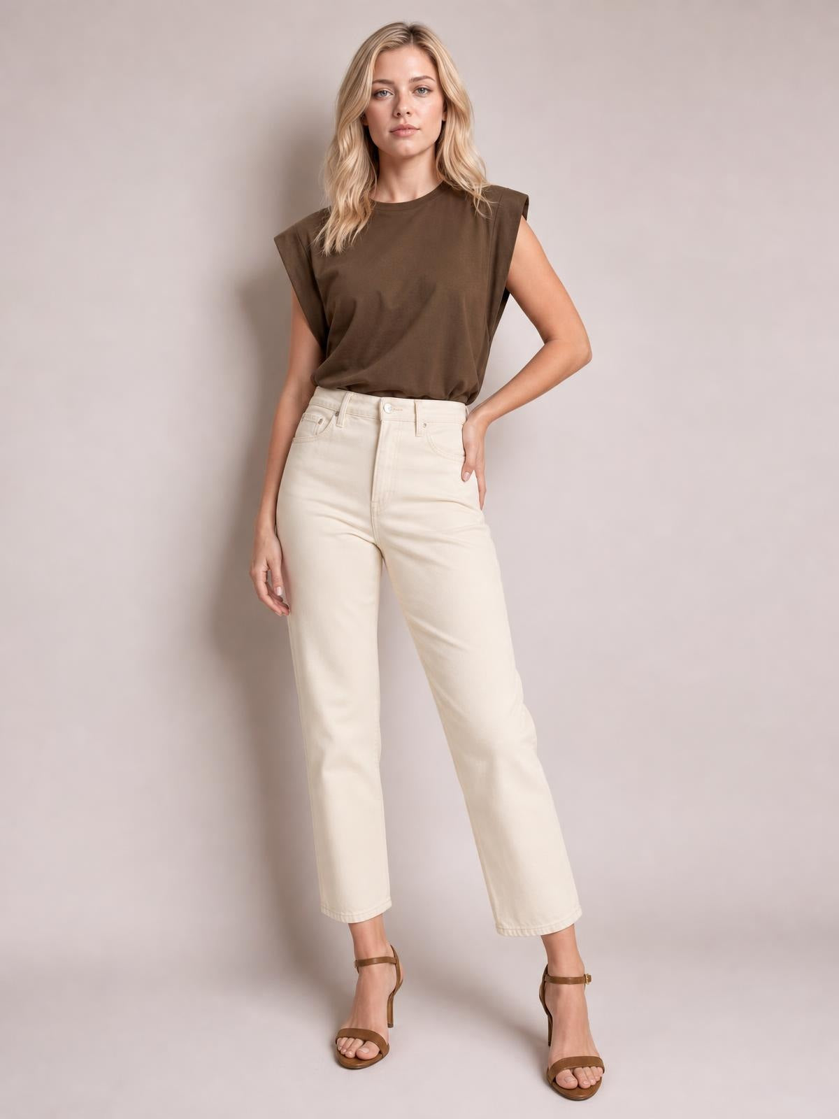 Model poses in a brown Florira round neck cap sleeve T-shirt with a relaxed silhouette, tucked into high-waisted cream straight-leg pants.
