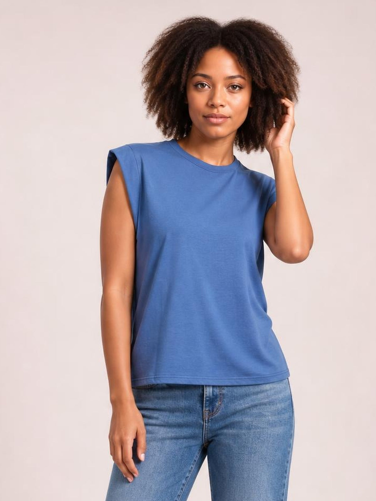 Model wears a blue Florira round neck cap sleeve T-shirt with a relaxed straight silhouette, standing casually with one hand touching her hair.