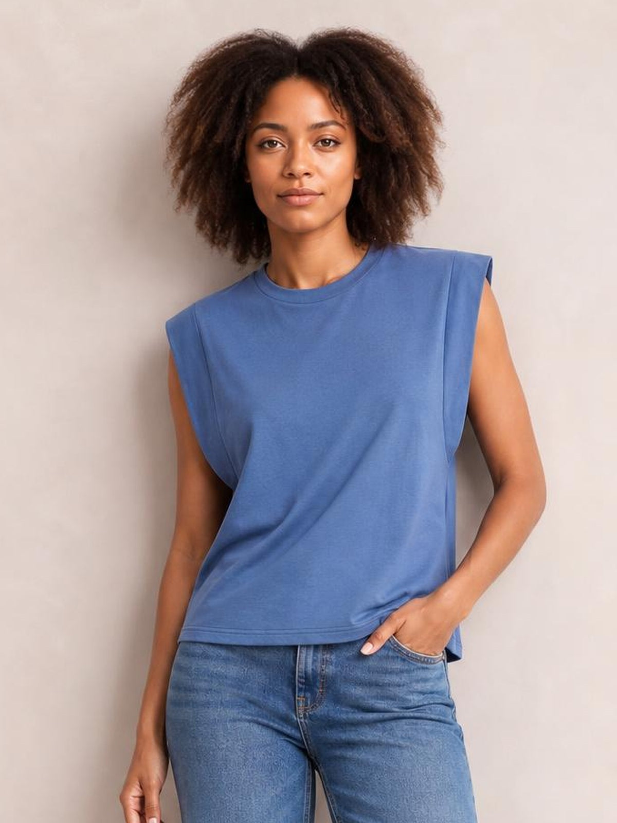 Model wearing a blue Florira round neck cap sleeve T-shirt with a relaxed silhouette, structured shoulders, and straight hem while posing with one hand in her jeans pocket.