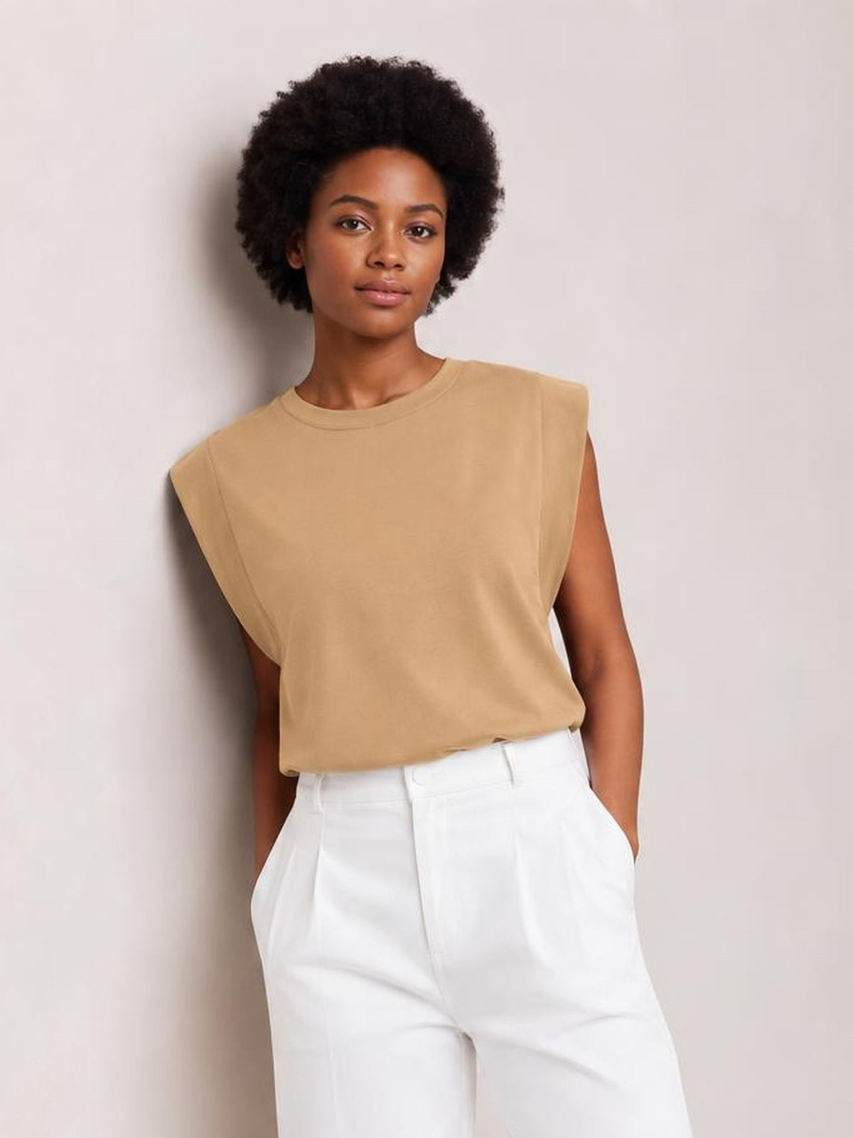 Model wearing a tan Florira round neck cap sleeve T-shirt with a relaxed silhouette, opaque fabric, and slightly stretchy construction, paired with white pants.