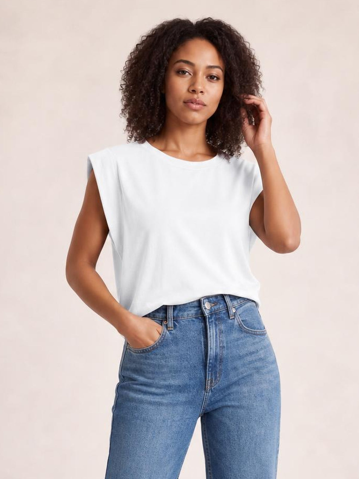 A model poses in a white Florira round neck cap sleeve T-shirt with a relaxed silhouette, slightly stretchy construction, and one hand in her jeans pocket.