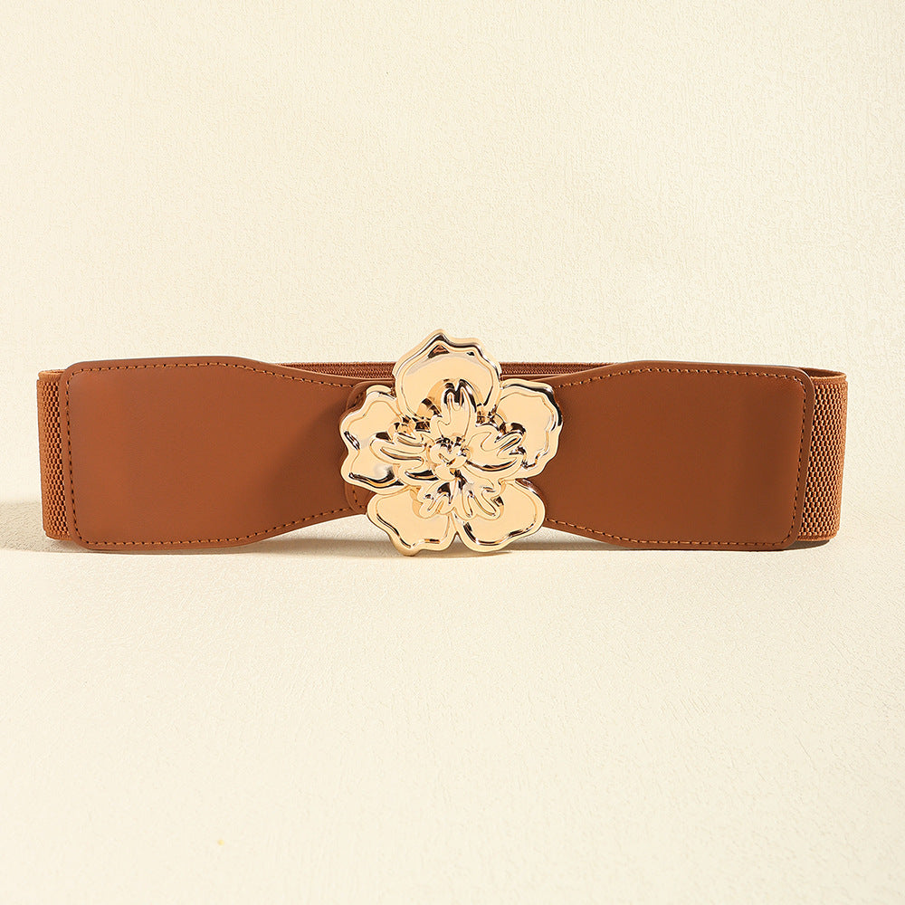 Brown wide elastic belt with a gently shaped silhouette, stitched edges, and a polished sculptural floral alloy buckle centered at the front.