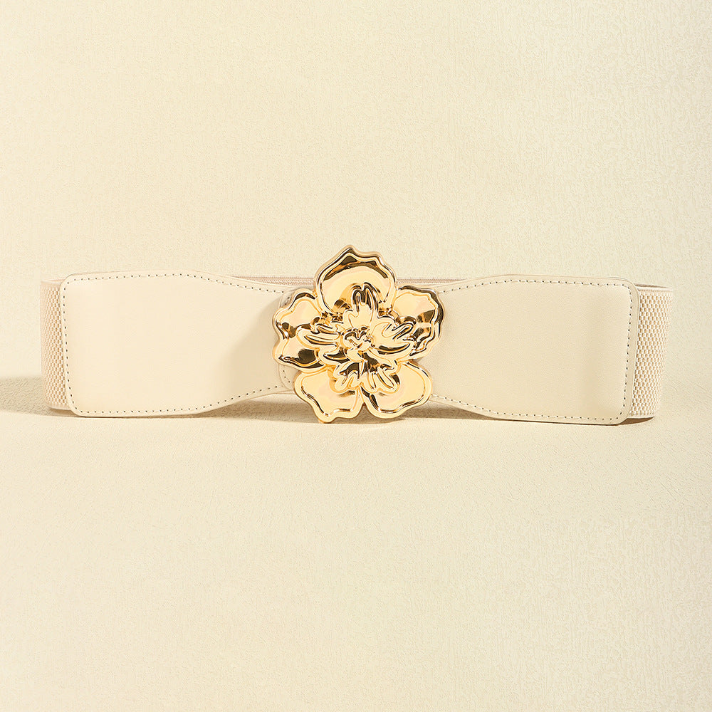 Cream wide elastic belt with a gently shaped silhouette, stitched edges, and a polished gold-tone alloy floral buckle at the center.