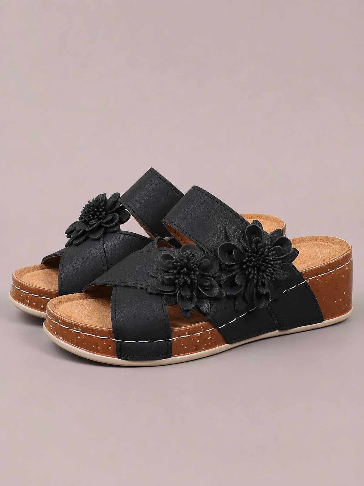 Black flower crisscross wedge sandals feature wide straps, layered floral embellishments, open toes, and mid-height brown platform wedges with textured soles.