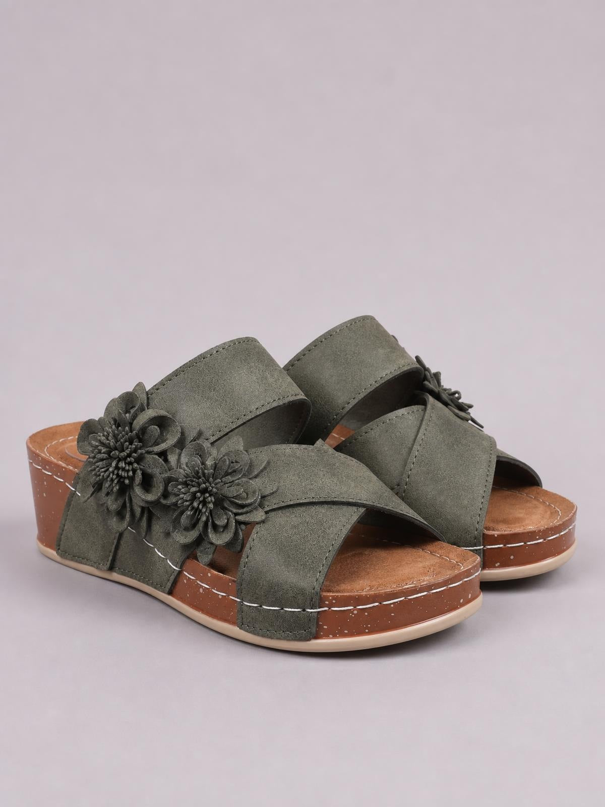 Olive green crisscross wedge sandals feature open toes, layered floral appliqués, wide stitched straps, and mid-height platform soles with textured sidewalls.