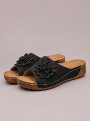 Black flower peep-toe wedge sandals feature perforated slip-on uppers, layered floral appliqués, and low brown wedge soles with contrast stitching.