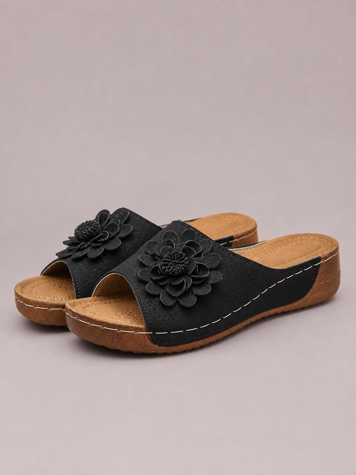 Black flower peep-toe wedge sandals feature perforated slip-on uppers, layered floral appliqués, and low brown wedge soles with contrast stitching.