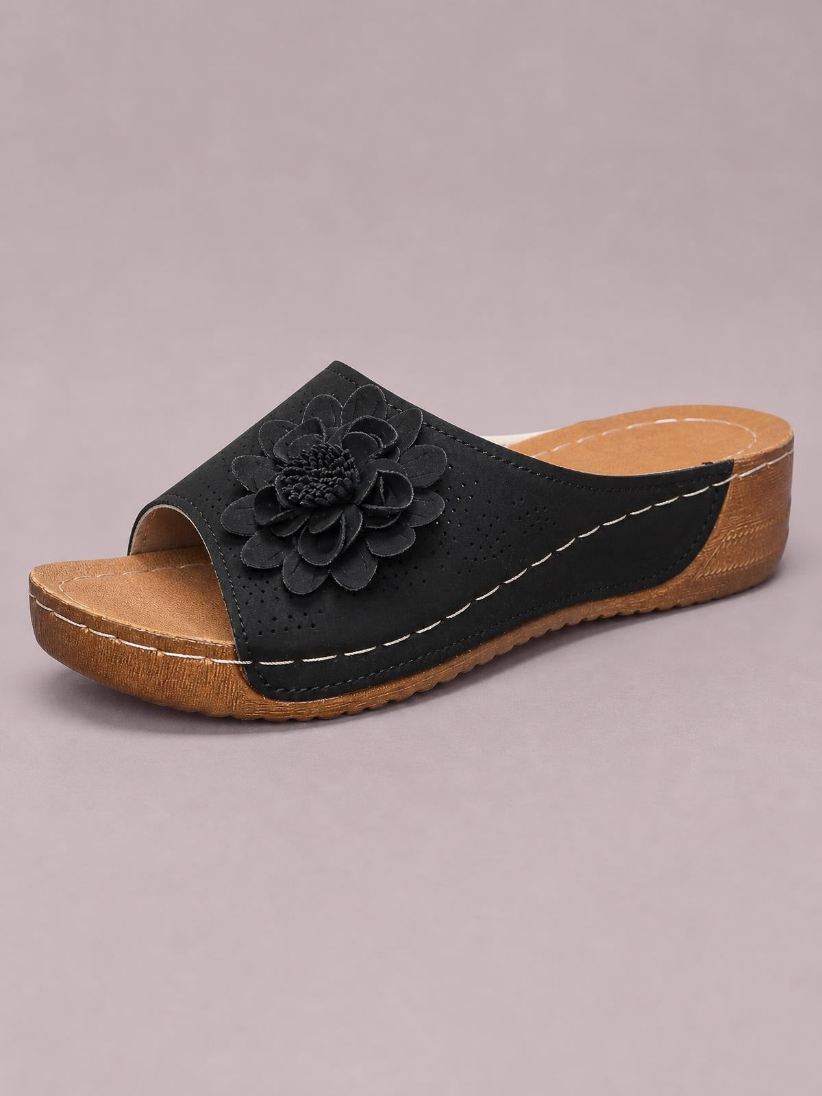 Black flower peep-toe wedge sandal with a perforated upper, layered floral embellishment, tan cushioned footbed, and low stitched wedge sole.