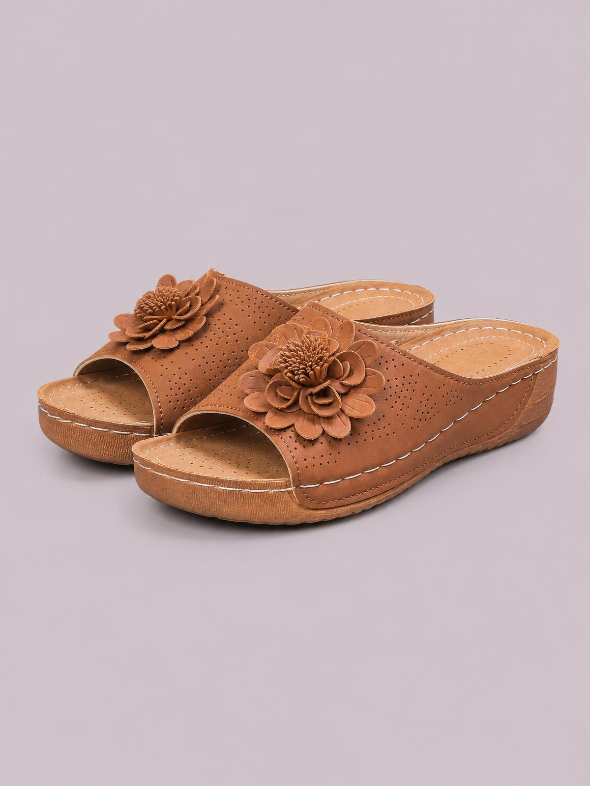 Brown flower peep toe wedge sandals feature perforated uppers, open backs, decorative floral appliqués, and low stitched wedge soles.
