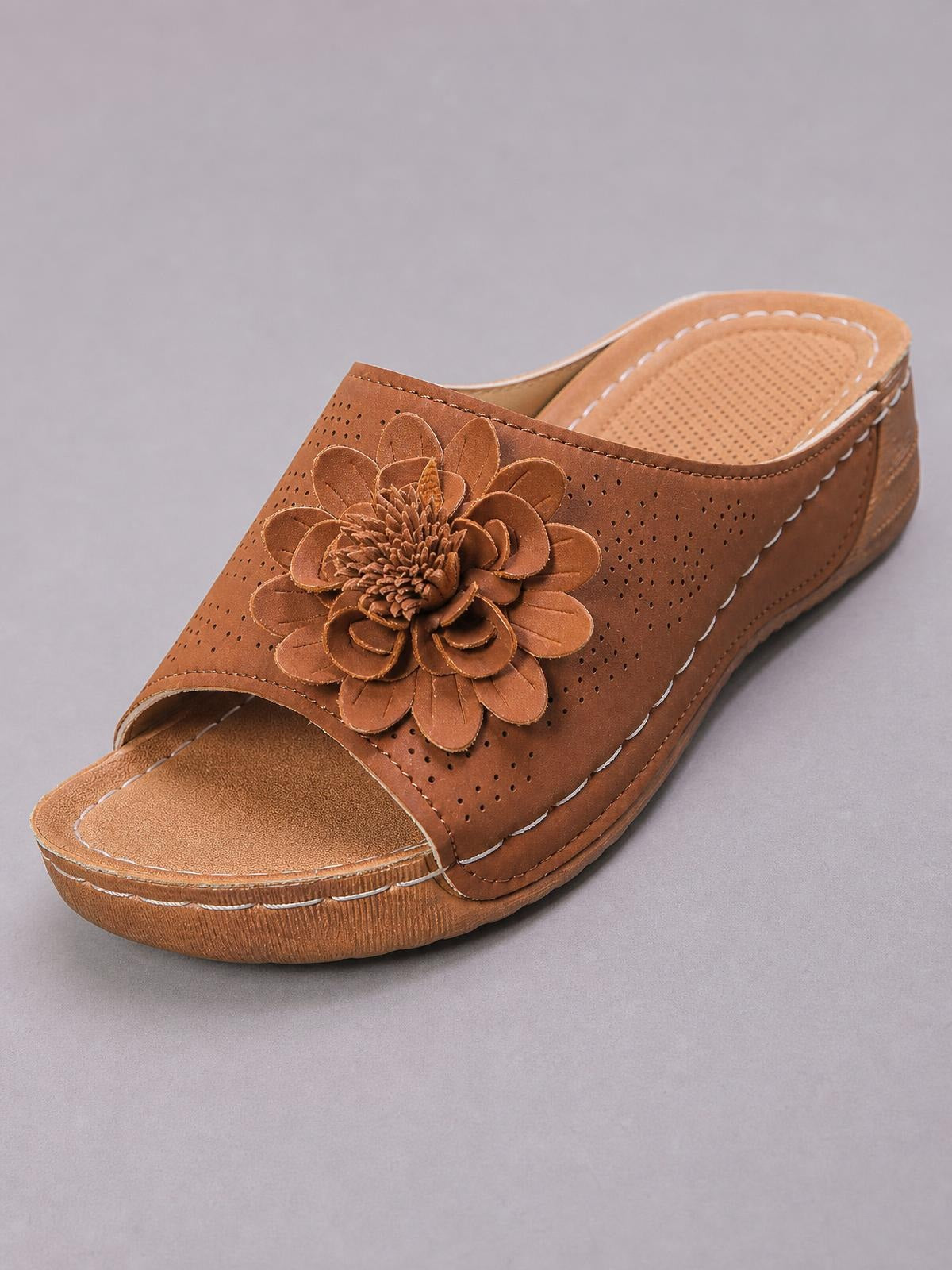 Brown flower peep toe wedge sandals in PU leather feature a perforated upper, open toe, decorative stitching, and a low wedge sole.