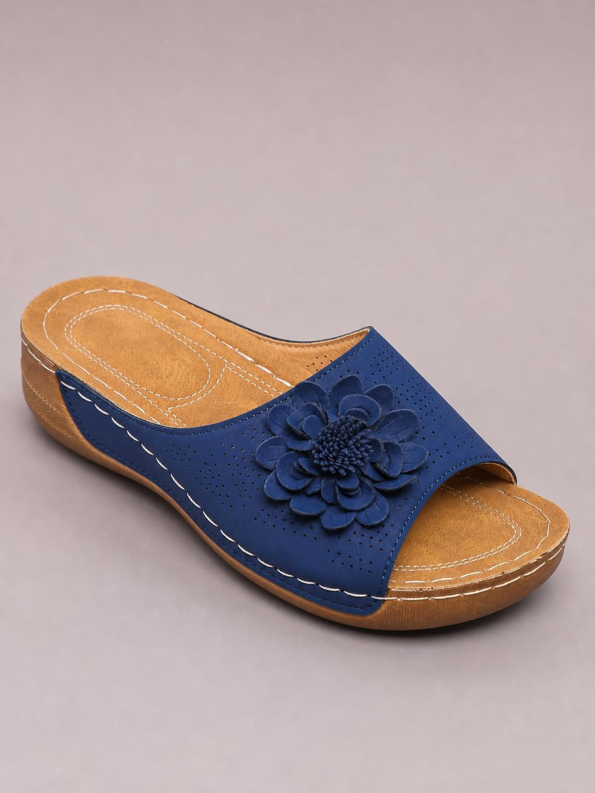 Navy blue flower wedge sandals feature a perforated slip-on upper, open toe, cushioned tan footbed, stitched detailing, and a low wedge sole.