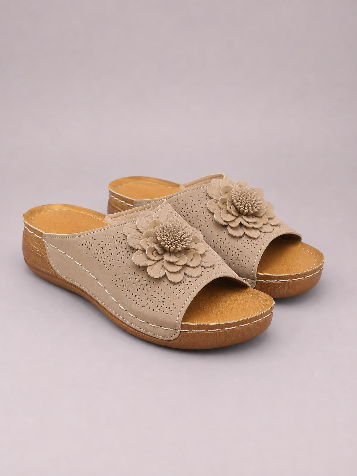Beige flower peep-toe wedge sandals feature perforated slip-on uppers, layered floral appliqués, open backs, low wedges, and stitched rubber soles.