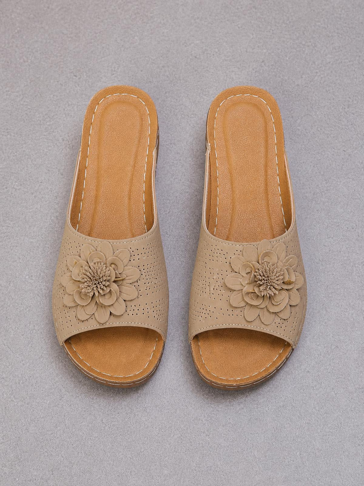Tan peep toe wedge sandals feature perforated uppers, layered flower appliqués, open backs, cushioned footbeds, and low wedge soles with contrast stitching.