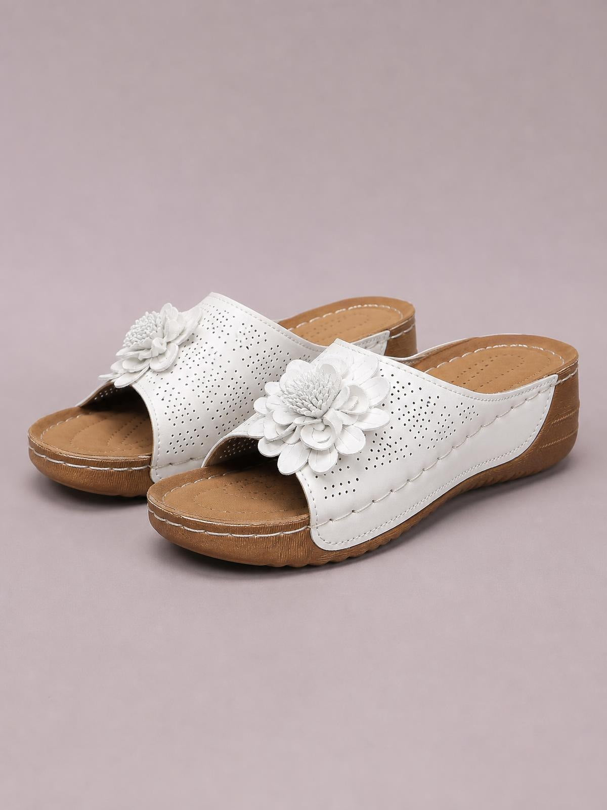 White flower peep toe wedge sandals feature perforated uppers, layered floral embellishments, open backs, and low brown wedge soles with stitched trim.