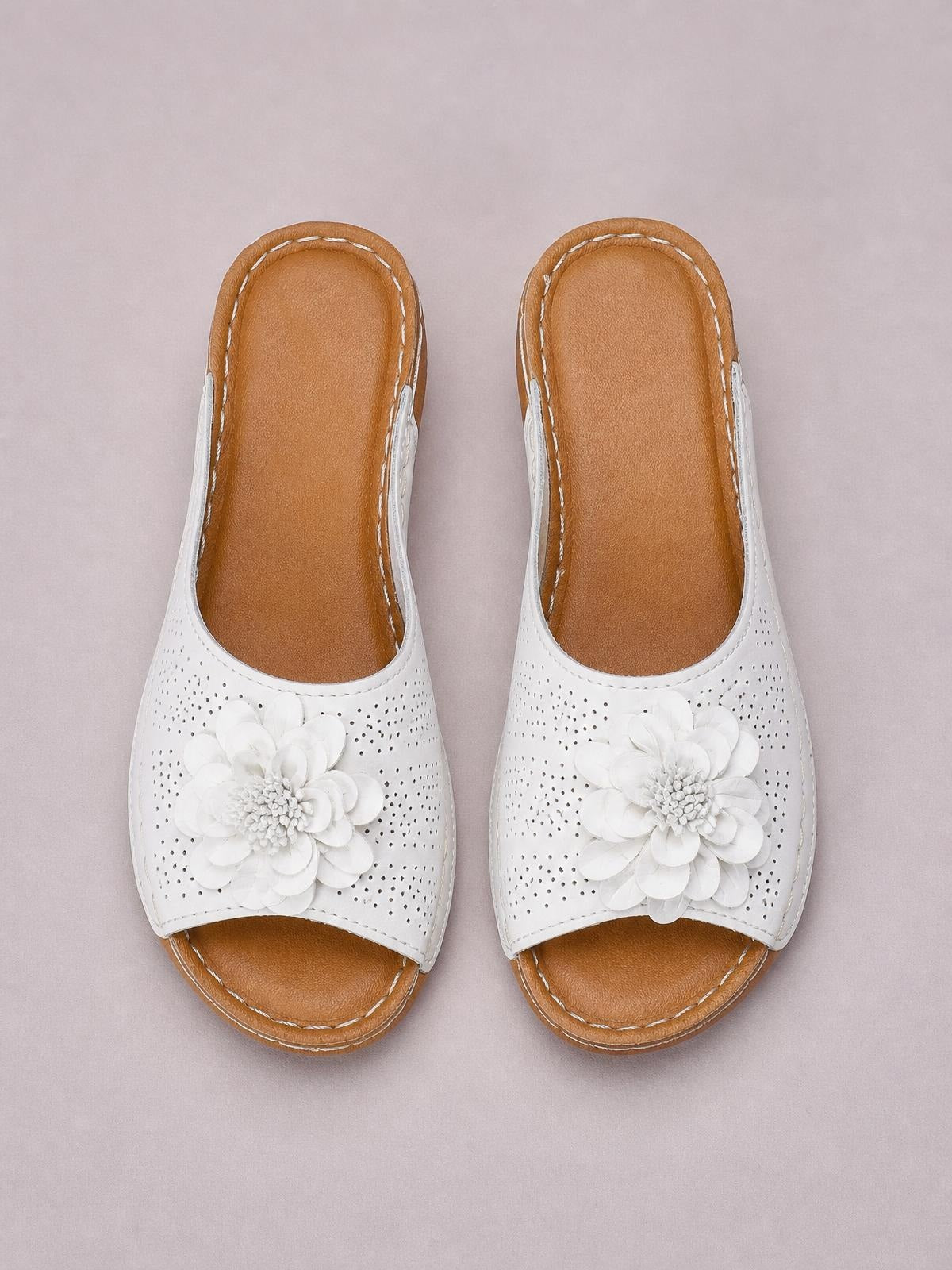 White flower peep toe wedge sandals feature perforated uppers, layered floral appliqués, tan cushioned footbeds, and low wedge soles.